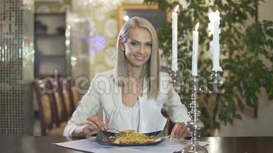 年轻的金发女郎穿着白色夹克，独自一人在高档餐厅吃意大利料理意大利面，做着滑稽的脸